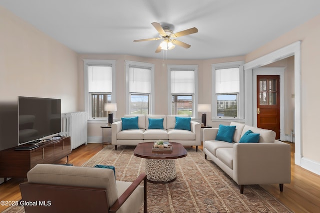living area with baseboards, wood finished floors, a ceiling fan, and radiator