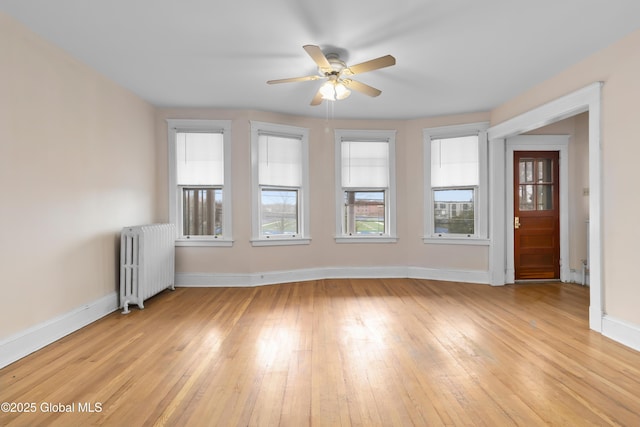 unfurnished room with radiator, light wood-style floors, ceiling fan, and baseboards