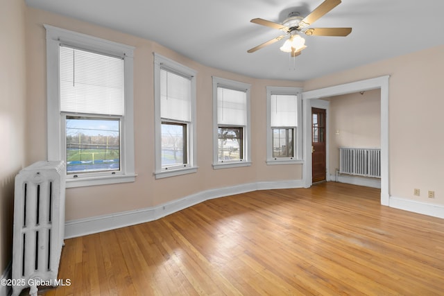 empty room featuring radiator heating unit, baseboards, light wood-style floors, and ceiling fan