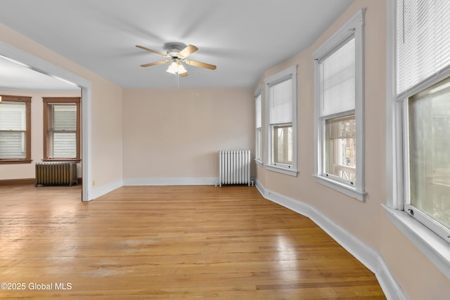 unfurnished room featuring a ceiling fan, radiator, and light wood finished floors