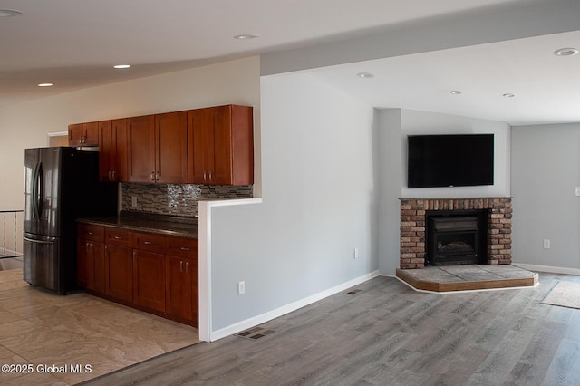 kitchen featuring freestanding refrigerator, light wood-type flooring, visible vents, dark countertops, and backsplash