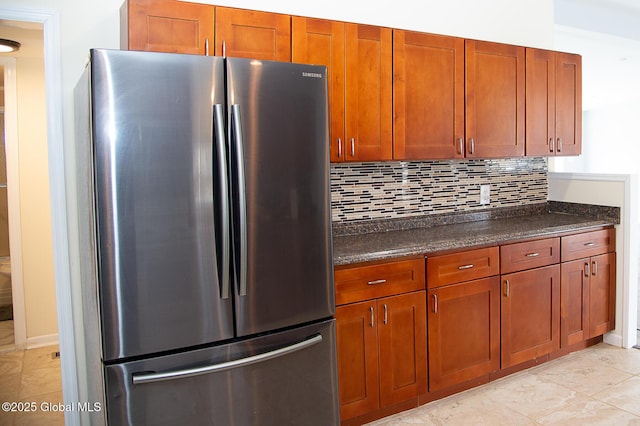 kitchen featuring tasteful backsplash, freestanding refrigerator, dark stone countertops, and brown cabinets