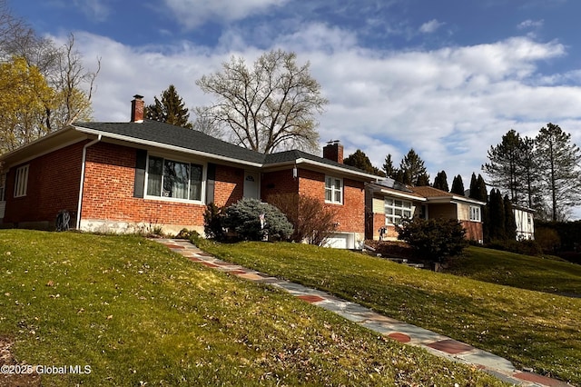 ranch-style house featuring a chimney, a front yard, and brick siding