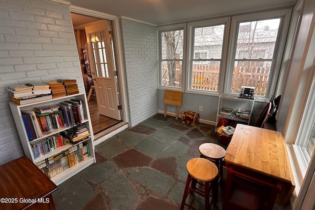 interior space featuring baseboards, stone finish floor, a wealth of natural light, and brick wall