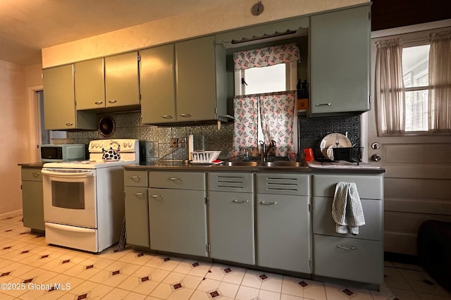 kitchen featuring backsplash, white range with electric stovetop, dark countertops, and a sink