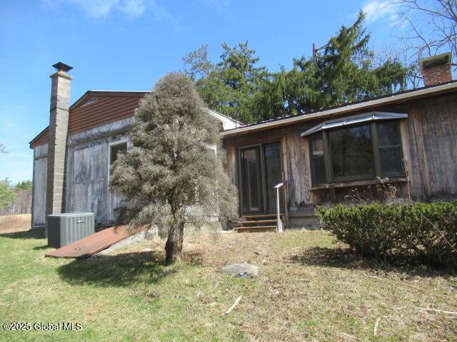 rear view of house featuring central AC unit, a yard, a chimney, and entry steps