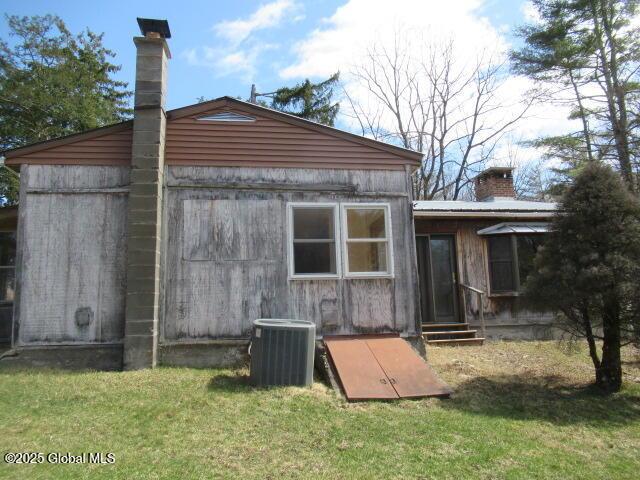 back of house featuring central AC unit, a yard, and a chimney