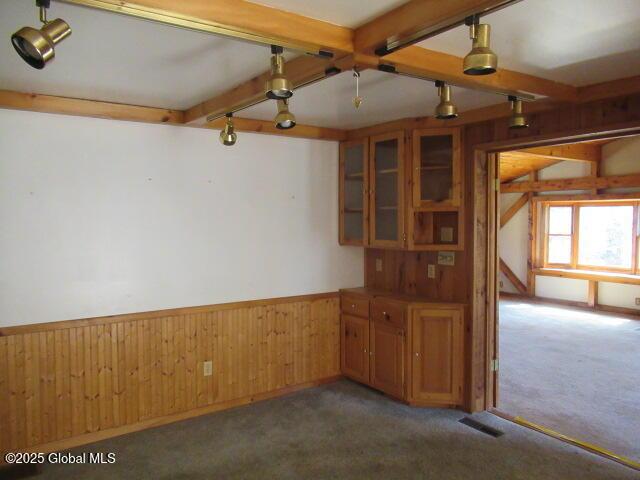 spare room featuring visible vents, beamed ceiling, wooden walls, a wainscoted wall, and carpet