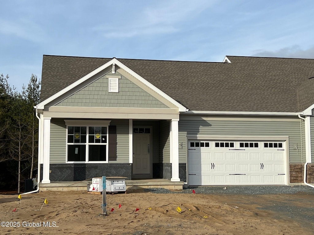 view of front of house featuring an attached garage, driveway, a shingled roof, and covered porch