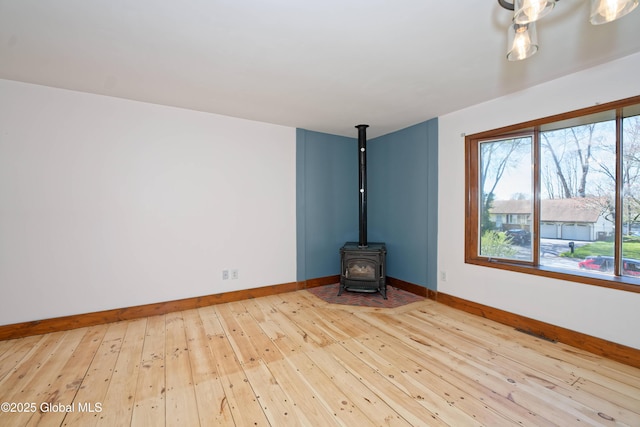 unfurnished living room with baseboards, a wood stove, and hardwood / wood-style flooring