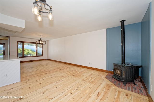 unfurnished living room with wood-type flooring, baseboards, an inviting chandelier, and a wood stove