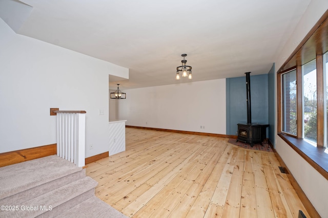 unfurnished living room with baseboards, a notable chandelier, a wood stove, and light wood-type flooring