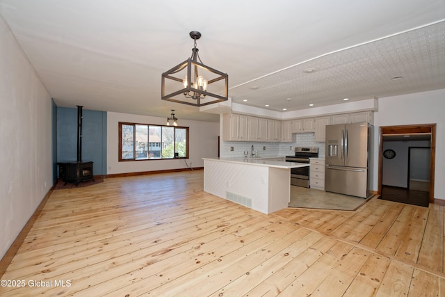 kitchen with appliances with stainless steel finishes, a sink, light wood-style flooring, tasteful backsplash, and visible vents