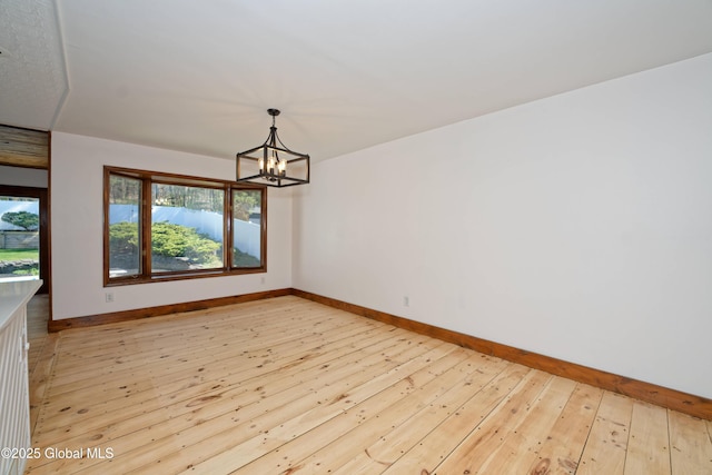 empty room featuring an inviting chandelier, baseboards, and light wood-type flooring