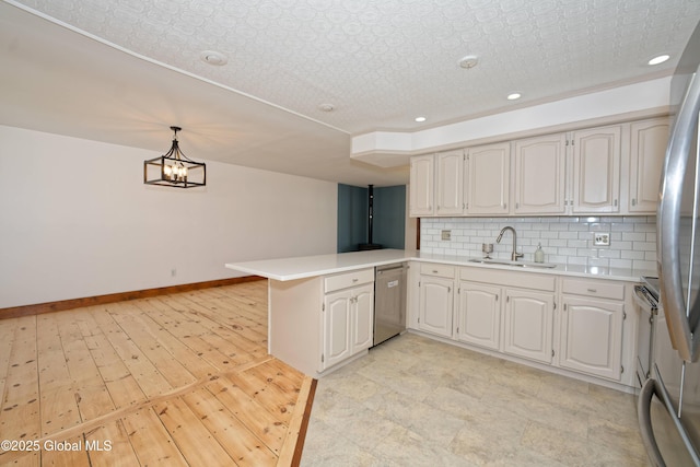 kitchen with a peninsula, light countertops, a sink, appliances with stainless steel finishes, and backsplash