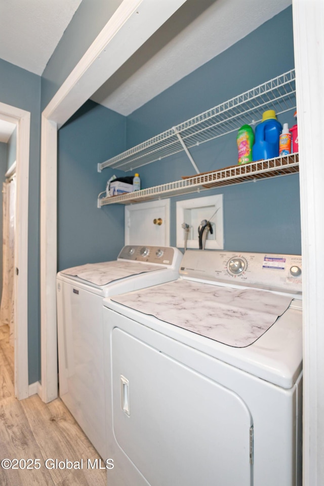 clothes washing area with laundry area, washer and clothes dryer, and light wood-style flooring