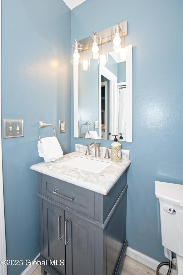 bathroom featuring vanity, baseboards, wood finished floors, and toilet