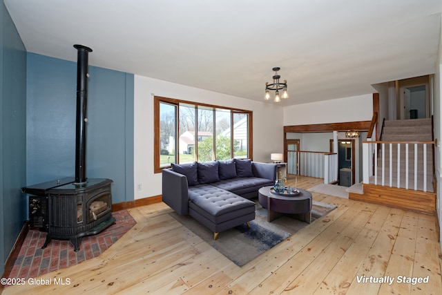 living room featuring a wood stove, wood-type flooring, a chandelier, baseboards, and stairway