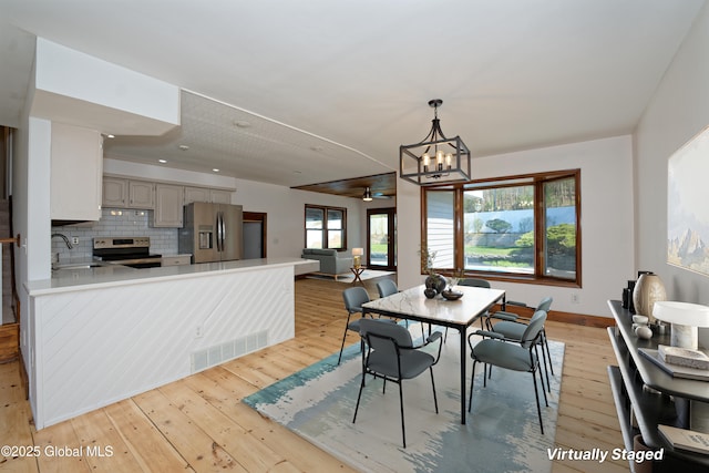 dining room with baseboards, visible vents, ceiling fan with notable chandelier, and light wood-type flooring