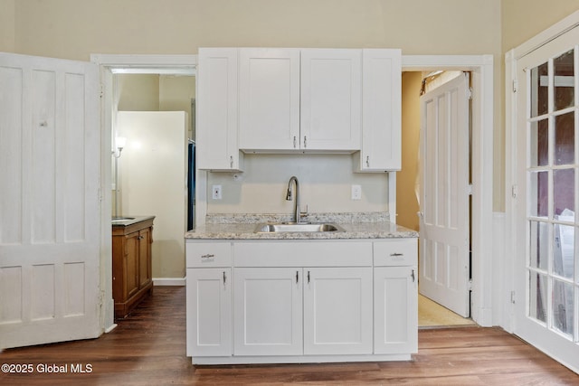 kitchen with a sink, white cabinets, wood finished floors, and light stone counters