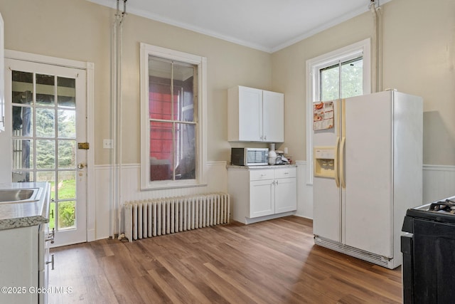 kitchen with radiator, white refrigerator with ice dispenser, black gas range oven, wainscoting, and crown molding