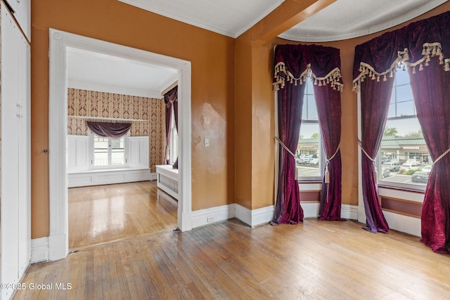 empty room with wood-type flooring, ornamental molding, and baseboards