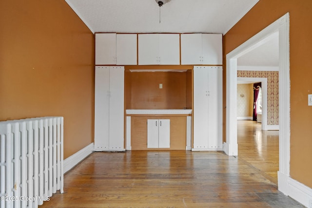 unfurnished living room with radiator heating unit, wood finished floors, and baseboards