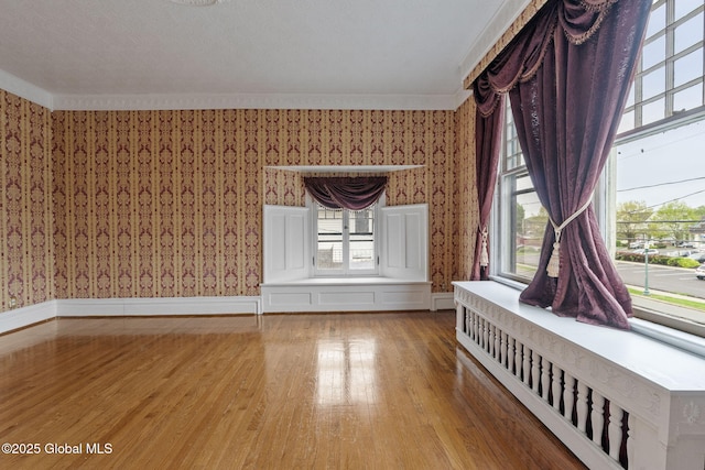 unfurnished living room with wallpapered walls, light wood-type flooring, crown molding, and healthy amount of natural light