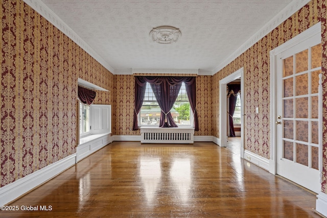 unfurnished living room with radiator heating unit, wallpapered walls, wood finished floors, ornamental molding, and baseboards