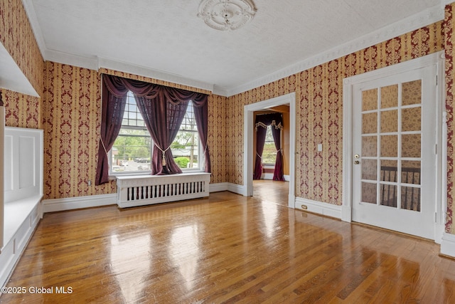 empty room with wallpapered walls, radiator heating unit, wood finished floors, a textured ceiling, and ornamental molding