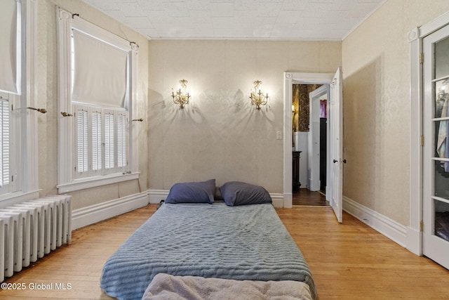 bedroom with radiator, light wood finished floors, baseboards, and ornamental molding