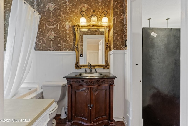 bathroom featuring wainscoting, wallpapered walls, toilet, vanity, and a shower with curtain