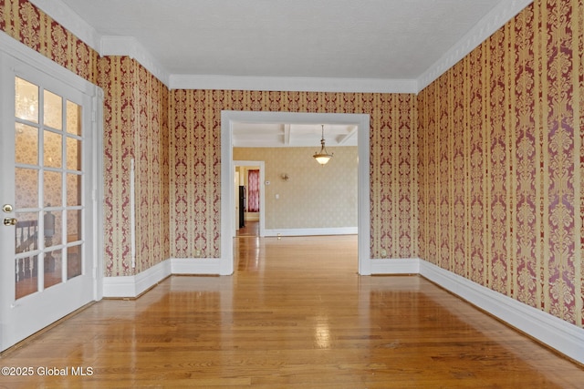 spare room featuring wallpapered walls, wood finished floors, baseboards, and crown molding