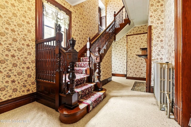 stairway with wallpapered walls, carpet, ornamental molding, radiator heating unit, and baseboards