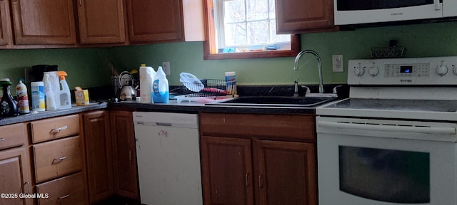 kitchen with a sink, brown cabinetry, dark countertops, and white appliances