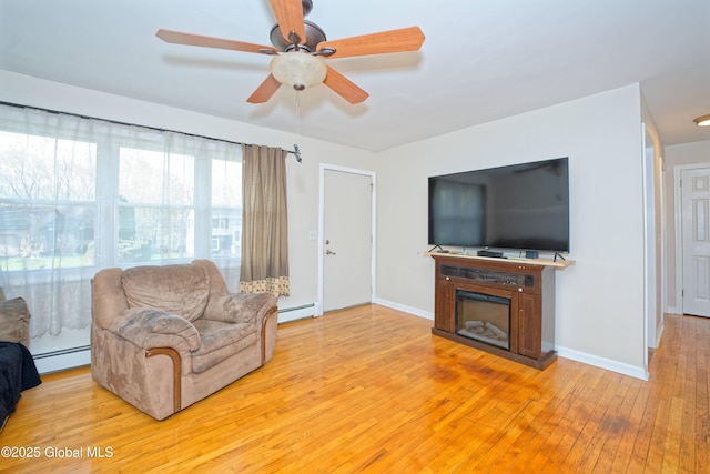 living area with ceiling fan, baseboards, a baseboard radiator, a glass covered fireplace, and light wood-style floors
