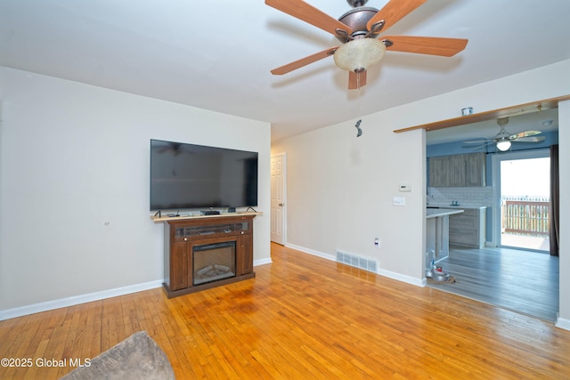 unfurnished living room with visible vents, a fireplace, baseboards, a ceiling fan, and light wood-style flooring