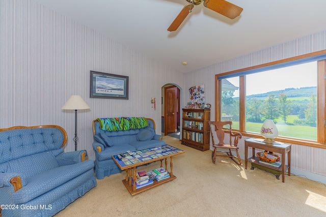 carpeted living area featuring wallpapered walls, arched walkways, lofted ceiling, and ceiling fan