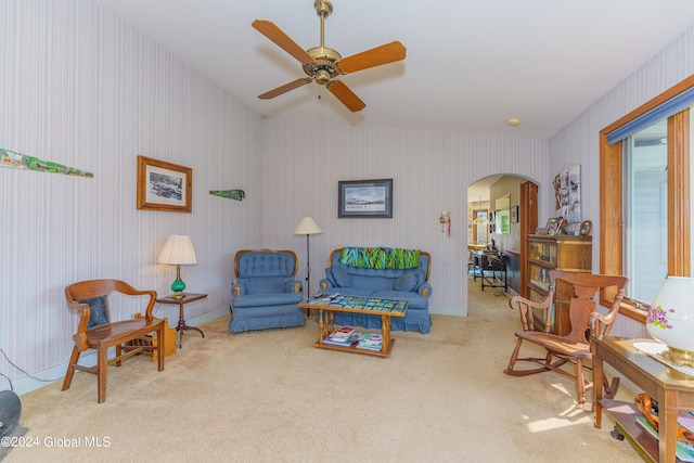 carpeted living area with wallpapered walls, arched walkways, and a ceiling fan