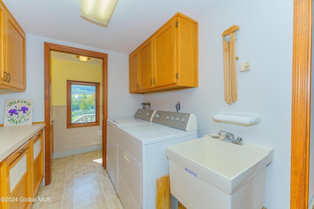 washroom featuring washing machine and clothes dryer, tile walls, a sink, cabinet space, and wainscoting