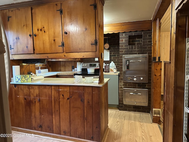 kitchen with electric stove, brown cabinets, light wood-style flooring, and crown molding