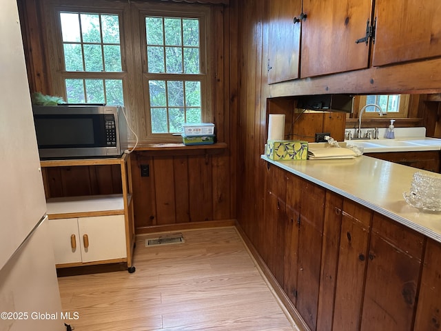 kitchen featuring stainless steel microwave, freestanding refrigerator, a sink, light wood-type flooring, and light countertops