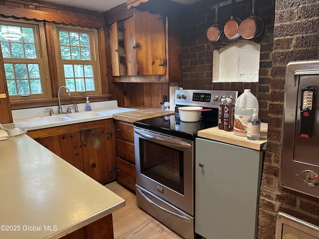 kitchen with stainless steel electric range, a sink, light countertops, and brown cabinetry