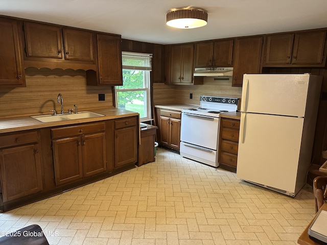 kitchen with white appliances, a sink, under cabinet range hood, and light countertops