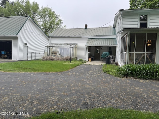 back of house featuring a chimney, metal roof, and a lawn