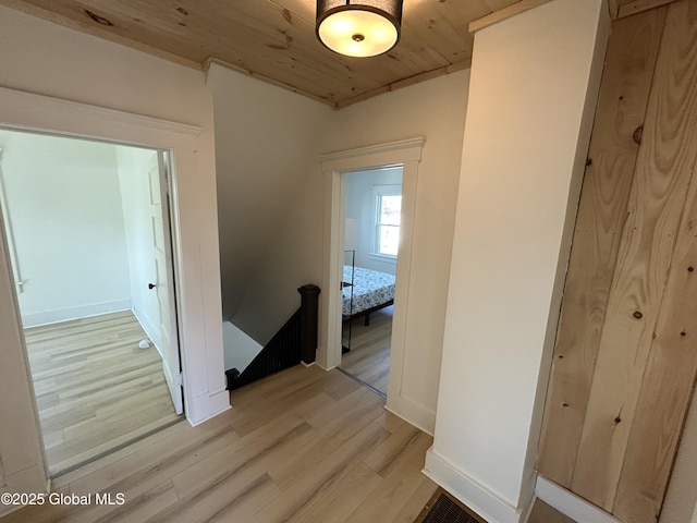 hall featuring light wood-style flooring, baseboards, an upstairs landing, and wooden ceiling