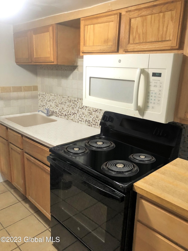 kitchen with electric range, a sink, light countertops, white microwave, and light tile patterned flooring