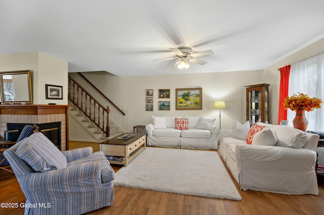 living area featuring a ceiling fan, wood finished floors, a fireplace, and stairs