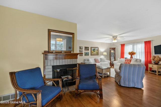 living area featuring a brick fireplace, wood finished floors, visible vents, and a ceiling fan