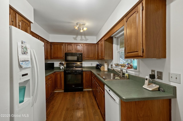 kitchen featuring brown cabinets, dark wood-style floors, dark countertops, a sink, and black appliances